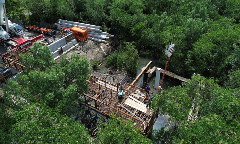 Imagem mostra grande guindaste junto a equipamento em área de mangue no local de construção da ponte Anêmonas