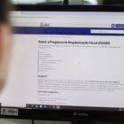 Pessoa olha para monitor de computador com informações sobre programa de regularização