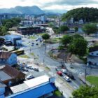 Imagem área mostra máquina trabalhando em rua, além de imóveis, rua pavimentada e vegetação