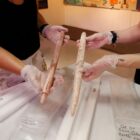 Duas mulheres, cujos rostos não aparecem, seguram duas lanças do acervo do museu do sambaqui