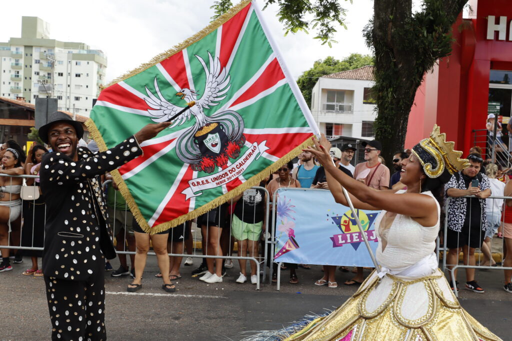 Mestre-sala e porta-bandeira exibem a bandeira da Unidos do Caldeirão na avenida