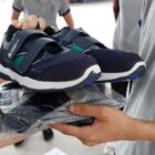 Imagem mostra mãos de pessoa adulta entregando pacote com roupa e um par de tênis azuis nas mãos de um adolescente