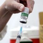 Dose de vacina é preparada com mãos segurando seringa e ampola