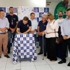 Imagem mostra várias pessoas em pé, lado a lado, que observam um homem no meio assinando uma folha sobre uma mesa