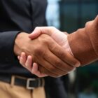 A imagem mostra um aperto de mãos entre uma pessoa branca e uma pessoa negra não identificadas