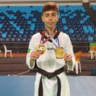 Jovem com uniforme de taekwondo posa para foto segurando duas medalhas que estão penduradas no pescoço