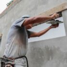 Homem usa ferramenta para espalhar concreto na abertura de uma janela em construção