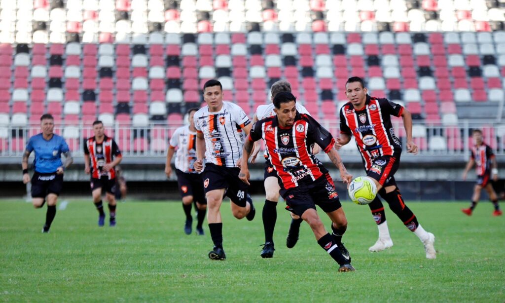 Homens uniformizados de times diferentes jogam futebol em um estádio