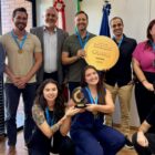 Homens e mulheres posam para foto e sorriem e seguram troféu