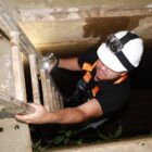 Homem usando capacete sobe uma escada de alumínio para sair de um espaço fechado no solo