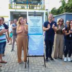 Pessoas aplaudem e posam para foto ao lado de placa de entrega de obra