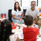 Homem e mulher estão sentados lado a lado em um sofá enquanto observam duas crianças brincando de costas para a câmera