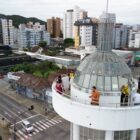 Imagem aérea mostra pessoas visitando a torre do Farol, com vista para a cidade