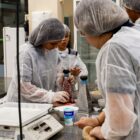 Alunas com jaleco e touca participam de oficina em laboratório de gastronomia