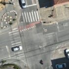 Imagem área mostra cruzamento em vias asfaltadas com alguns carros em movimento