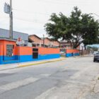 Rua com asfalto gasto, com empresa e comércio, carros estacionados