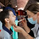 Uma mulher usando máscara ilumina a boca aberta de um menino para avaliar a sua saúde bucal