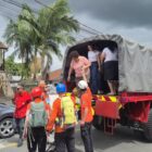 Pessoas vestidas de laranja e com capacete ajudam mulher idosa a descer da carroceria de um caminhão dos bombeiros