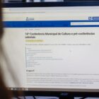 Mulher olha para tela de computador com informações sobre conferência de cultura