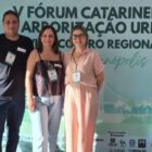 Um homem e duas mulheres estão em pé, posando para a foto, na frente de um painel sobre arborização urbana