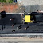 Imagem aérea de uma rua sendo asfaltada com máquinas e homens trabalhando