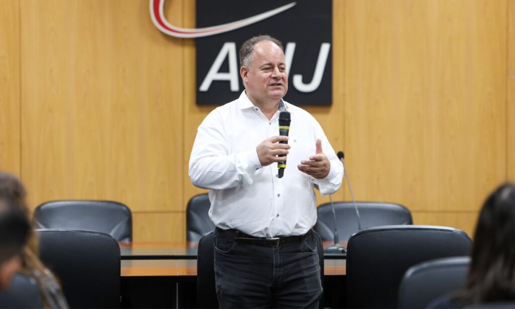 Homem de camisa branca segura microfone durante apresentação