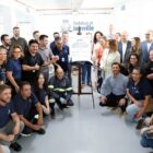 Várias pessoas, algumas em pé e outras agachadas, posam para a foto ao lado de uma placa de metal sobre a modernização da ETA Cubatão