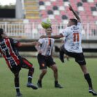 Três homens disputam uma bola alta em campo de futebol