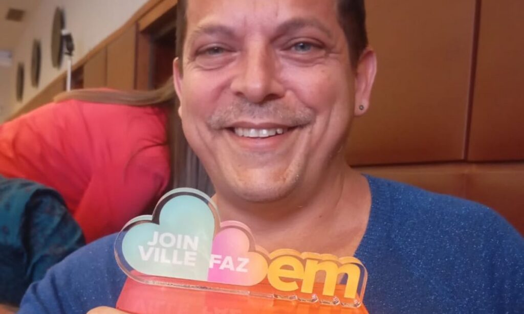 Um homem sorri para a foto enquanto segura o troféu Joinville Faz Bem