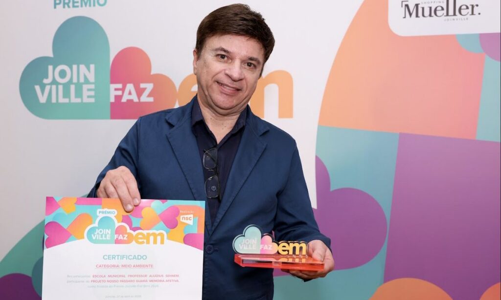 Homem sorri para a câmera enquanto segura um certificado e o troféu do Joinville Faz Bem