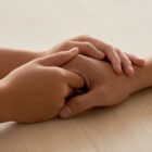 Imagem mostra duas mãos de duas pessoas diferentes dadas sobre uma mesa