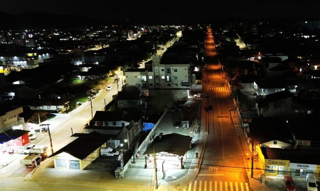 Imagem aérea feita à noite mostra uma rua com iluminação modernizada e outra com iluminação antiga