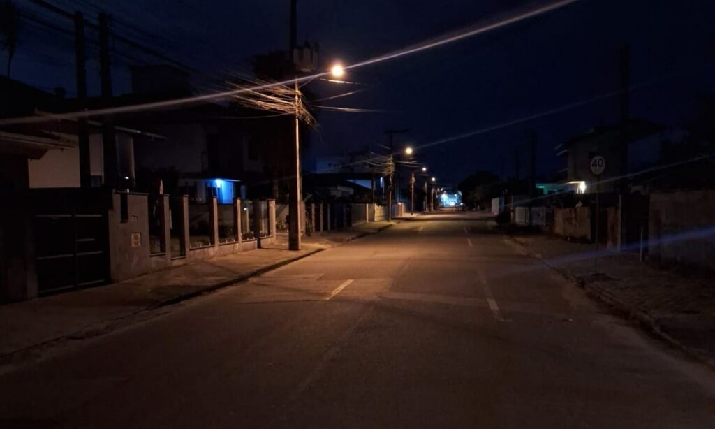 Rua pavimentada com iluminação noturna ainda não modernizada, mais escura