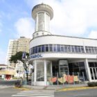 Prédio branco com janelas e torre de vidro na esquina entre ruas