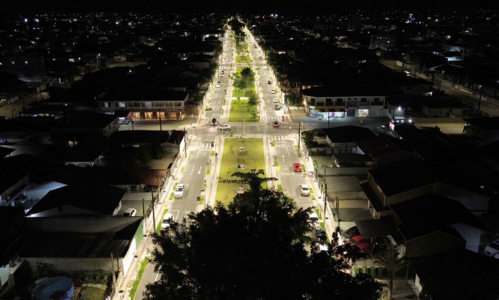 Imagem aérea noturna de um passeio publico, com iluminação em destaque, área de gramado e árvores