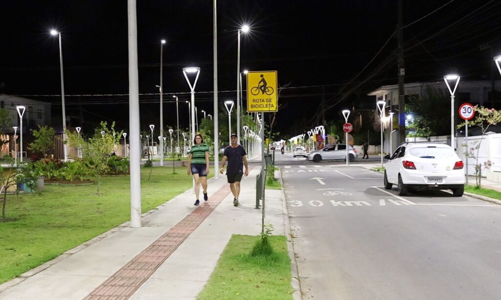 Homem e mulher caminham em calçada de passeio público durante a noite