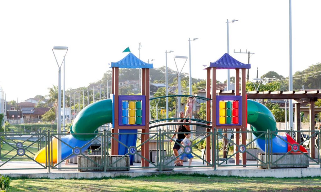 Duas crianças brincam em uma área de parquinho com brinquedos coloridos