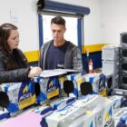 Mulher ao lado de homem confere papéis em loja de baterias de carro