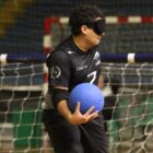 Atleta em campo, com os olhos vendados e com uma bola azul na mão