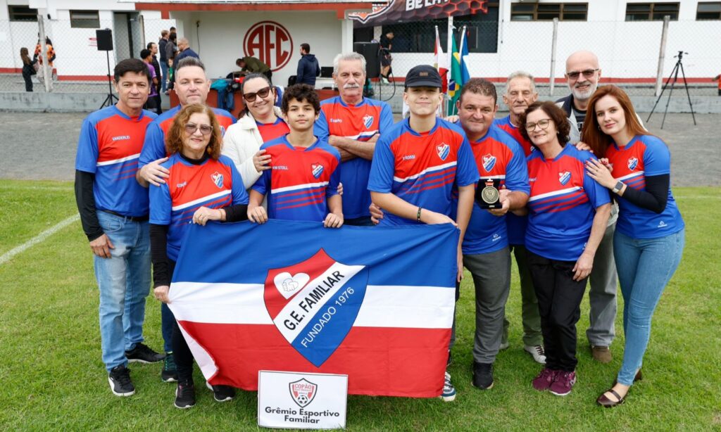 Pessoas de uniforme azul e vermelho seguram uma bandeira e posam juntas para foto