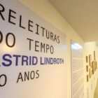 Imagem mostra sala com painel escrito Releituras do tempo, Astrid Lindroth 50 anos