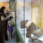 Uma mulher idosa, uma mulher e jovem e uma menina observam uma exposição no Museu Arqueológico de Sambaqui
