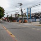 Imagem mostra rua pavimentada com árvores e construções às margens