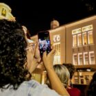 Mulher fotografa prédio histórico iluminado durante passeio noturno ao lado de outras pessoas