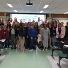 Imagem mostra dezenas de pessoas reunidas, em pé, posando para a foto, na frente de uma sala de aula