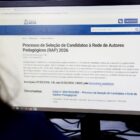 Mulher vê monitor de computador com informações sobre processo de seleção
