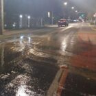 Rua pavimentada está molhada. Ao fundo, há um carro em movimento