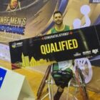 Homem jovem está sentado em cadeira de rodas. Ele segura uma placa horizontal que diz qualified.