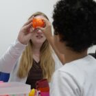 Terapeuta e criança seguram juntas peça de plástico em formato de fruta