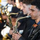 Imagem mostra músicos vestidos de preto tocando instrumentos de sopro